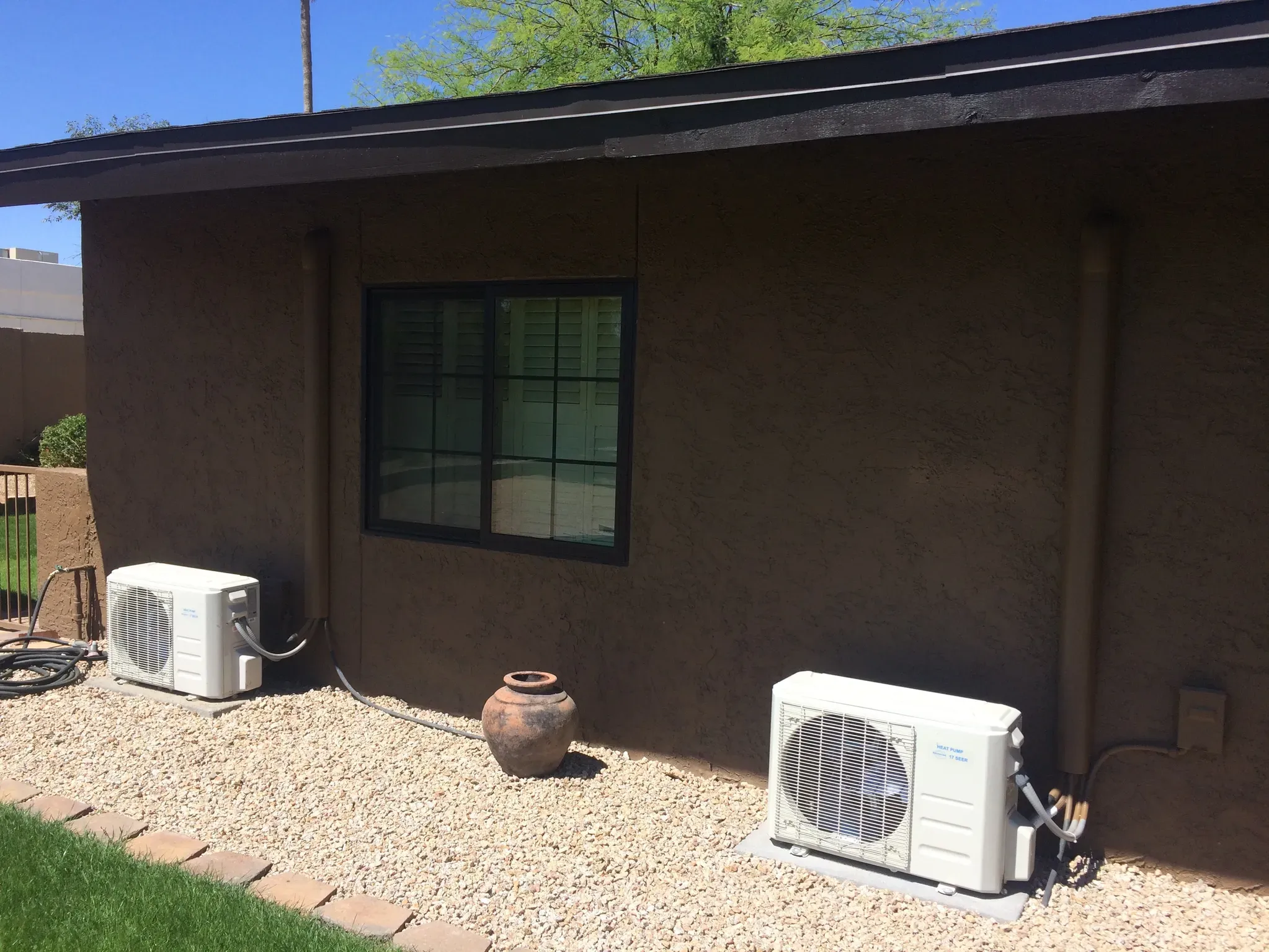 Two mini split outdoor condenser units installed on gravel pad on side of Arizona home — whole home conversion